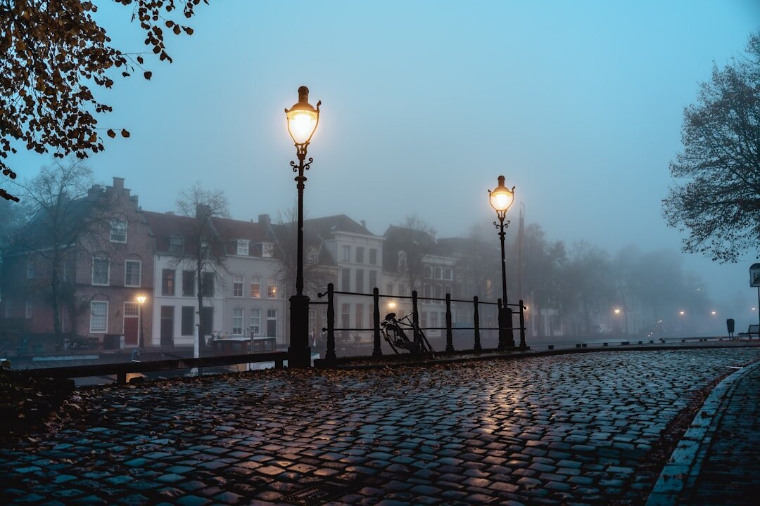 Foggy cobblestone street at night with a single lit street lamp, evoking a mystery novel scene