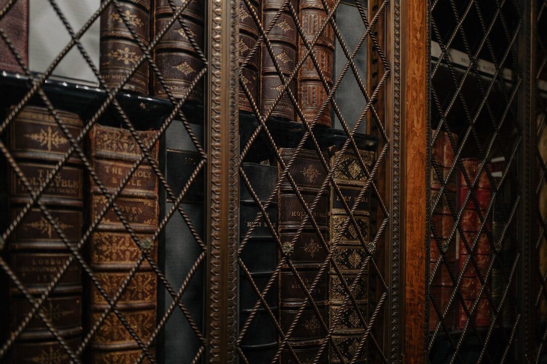 Tall wooden bookshelf filled with old hardcover novels in a warmly lit study